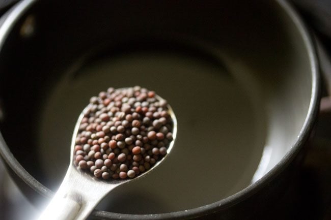 adding mustard seeds to hot coconut oil in a tempering pan for making tempering for kalan. 