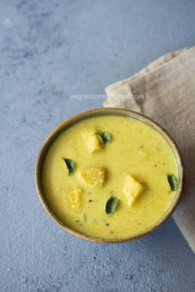 kalan garnished with curry leaves and served in a brown ceramic bowl. 