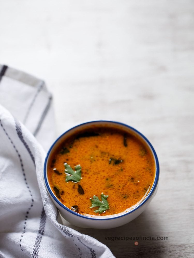 tomato saar garnished with coriander leaves and served in a blue rimmed white ceramic bowl with text layover.