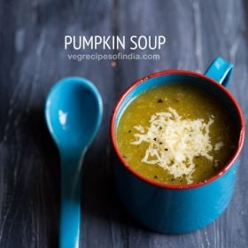 pumpkin soup topped with cheese and served in a blue soup mug with a blue spoon on a dark blue wooden board