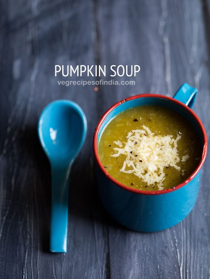 pumpkin soup topped with cheese and served in a blue soup mug with a blue spoon on a dark blue wooden board