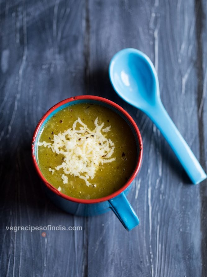 pumpkin soup topped with cheese and served in a blue soup mug with a blue spoon on a dark blue wooden board.