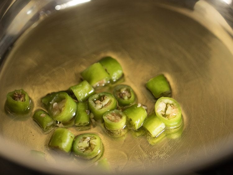 chopped green chilies added to hot peanut oil in a large pan for rishi panchami bhaji.
