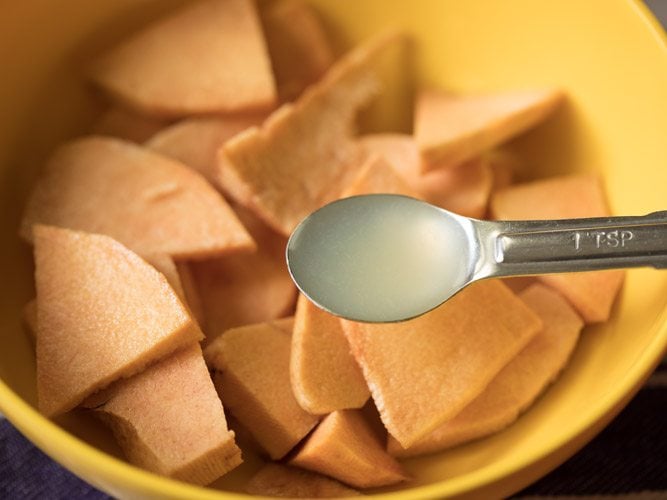 lemon juice being added with a measuring spoon into the bowl with yam slices