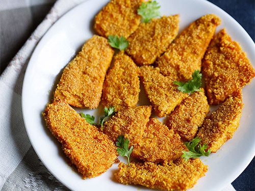 fried yam arranged on a white plate and garnished with coriander leaves placed on a grey and white napkin