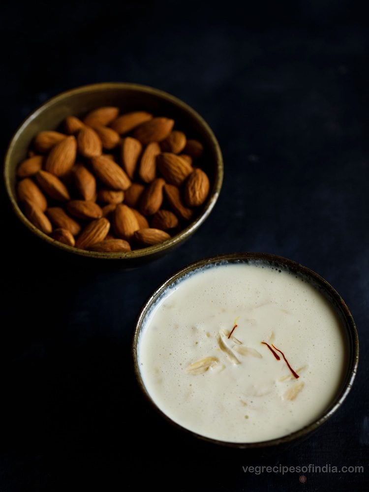 badam kheer served in a bowl with a bowl of almonds kept on the top left side and text layover. 