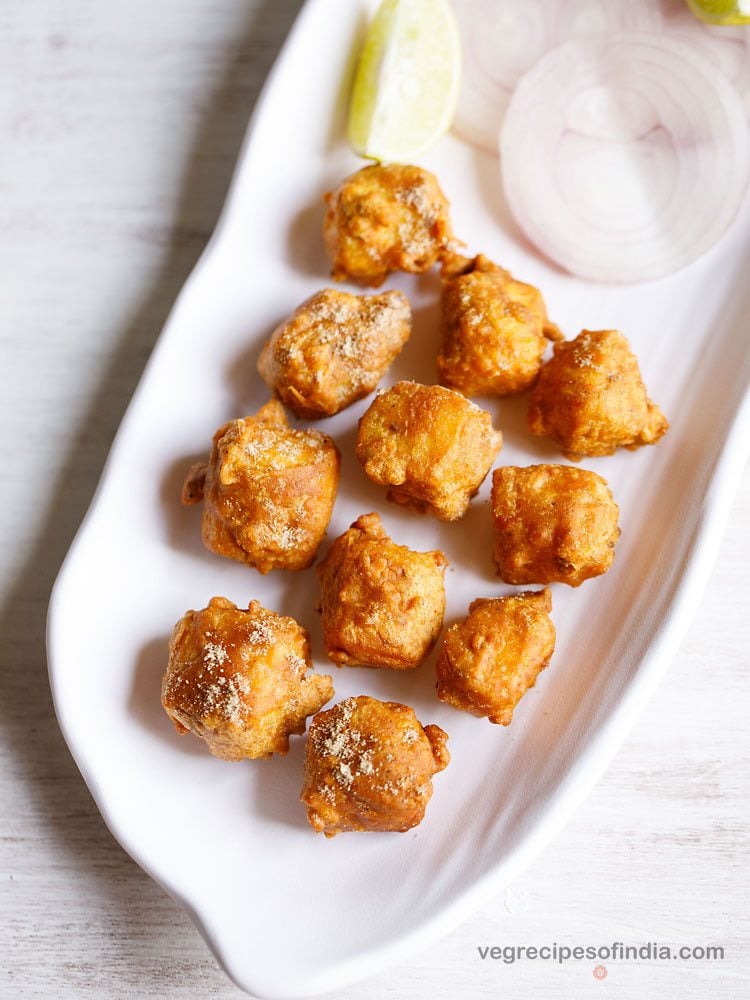 paneer koliwada served with onion rings and lemon wedge on a white platter. 