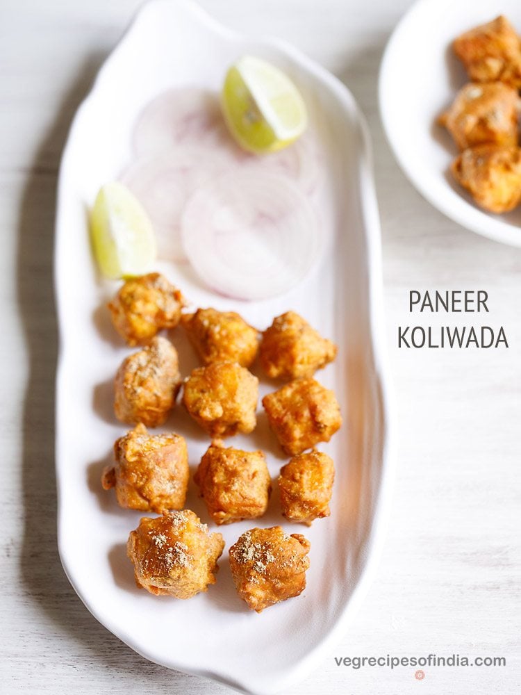 paneer koliwada or fried paneer cubes on a white platter with onion slices and lemon wedges.