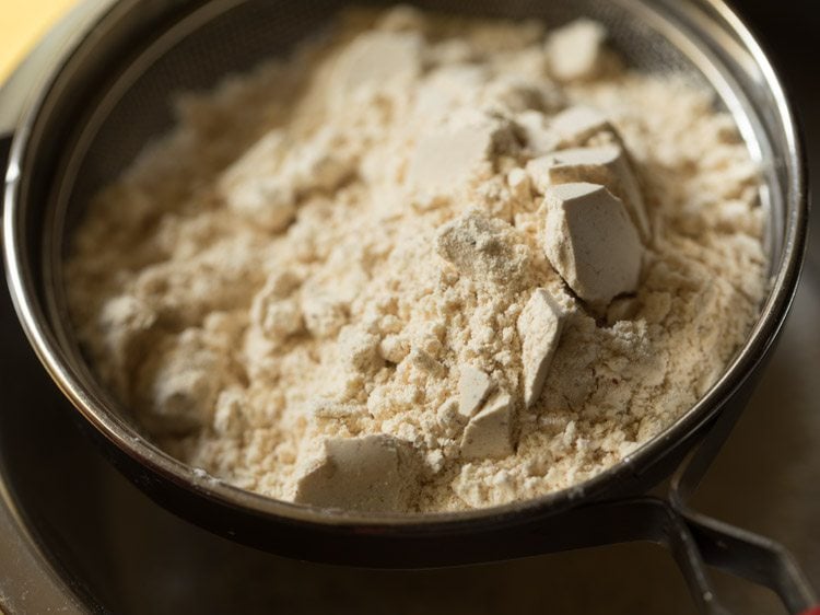 prepared spiced chana dal powder added in the sieve for ribbon pakoda recipe. 