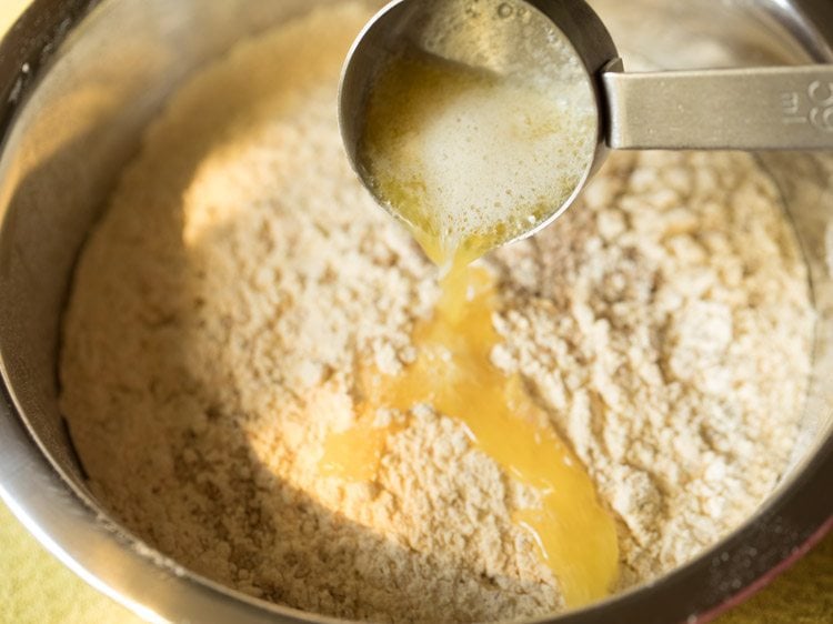 adding melted butter in the sifted mixture for making the dough for ribbon murukku. 