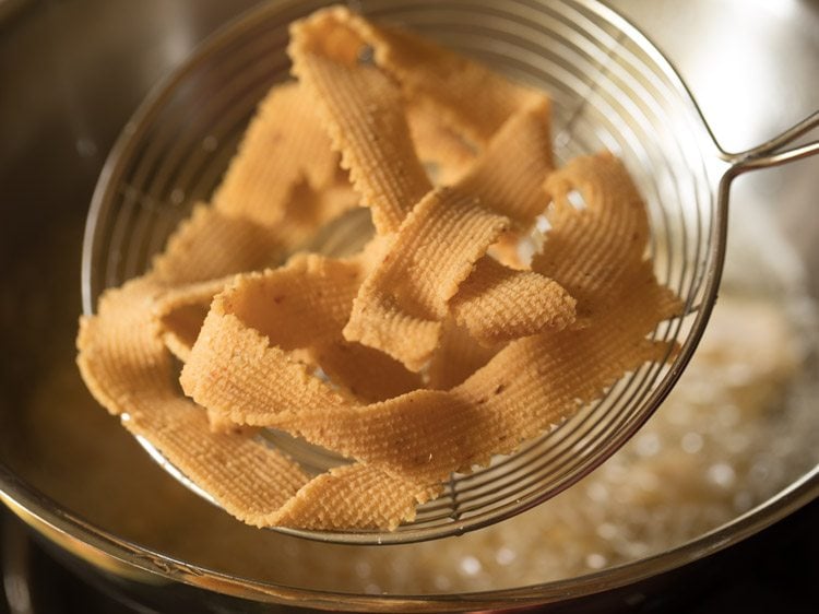 removing fried ribbon murukkus with a slotted spoon. 