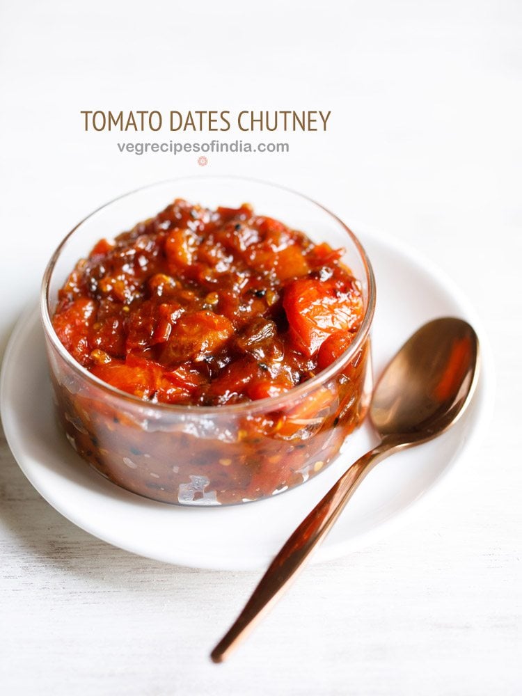 tomato khejur chutney served in a glass bowl kept on a white plate with a spoon on the right side and text layovers.