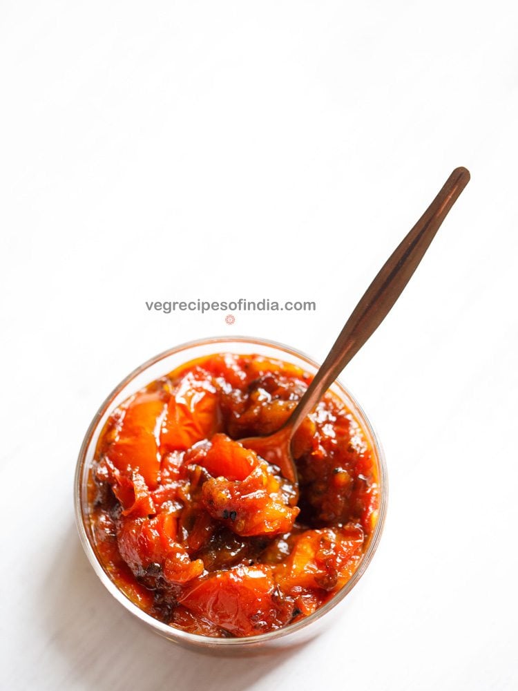 tomato khejur chutney served in a glass bowl with a spoon inside it and text layover. 