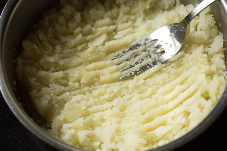 mashing cooked potatoes with a fork for making bread patties. 