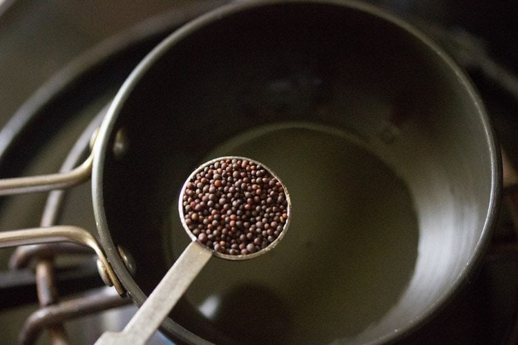 adding mustard seeds to hot oil in a small pan for making tempering for bread patties. 