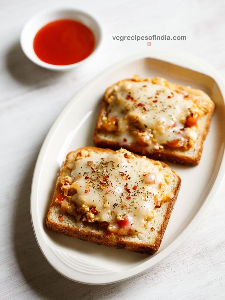 paneer cheese toast served on a white platter with a small bowl of tomato ketchup kept on the top left side and text layovers. 