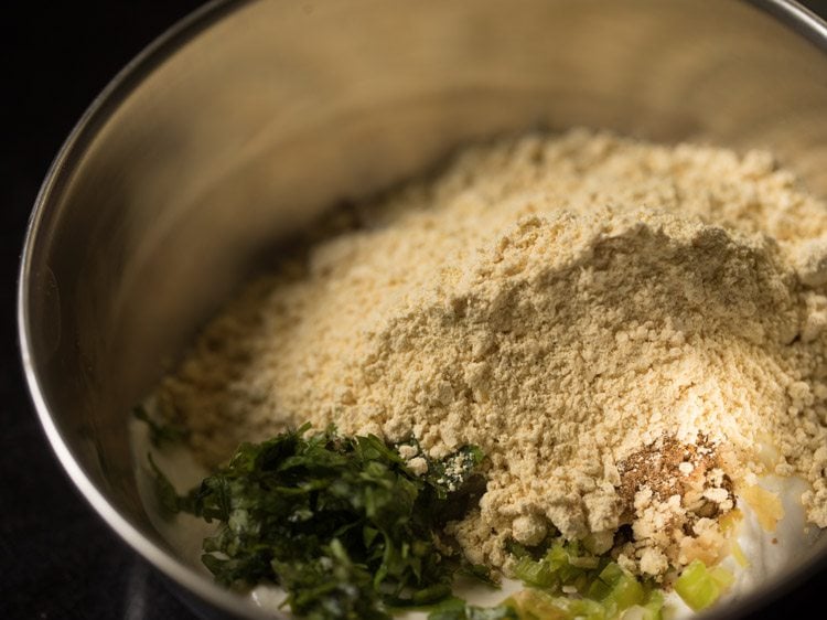 chopped onions, ginger, green chilies, coriander, cumin, besan and curd in a bowl