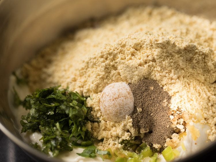 chopped onions, ginger, green chilies, coriander, cumin, besan, pepper and curd in a bowl