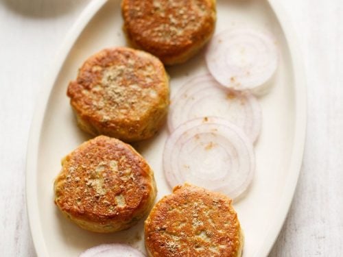 dahi ke kabab on a platter with some sliced onion rounds and a sprinkling of chaat masala