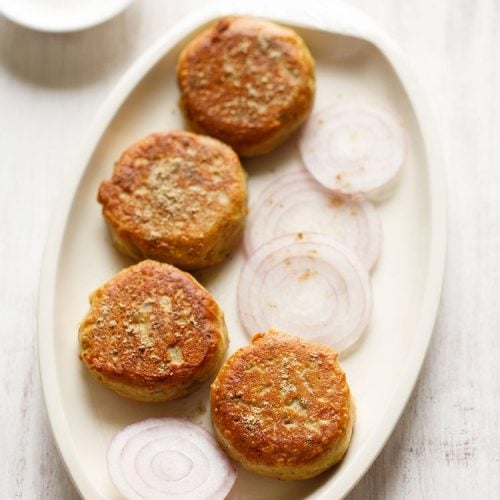 dahi ke kabab on a platter with some sliced onion rounds and a sprinkling of chaat masala