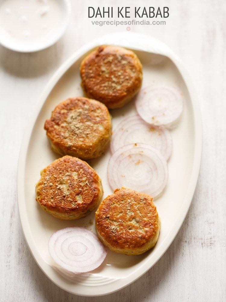 dahi ke kabab on a platter with some sliced onion rounds and a sprinkling of chaat masala