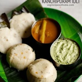 kanchipuram idli served on a banana leaf placed on a green colored plate with a bowl of coconut chutney and a bowl of sambar kept on the right side on the plate and text layovers.