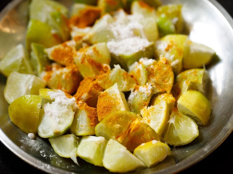 turmeric powder and salt added to chopped lemon pieces on a plate. 