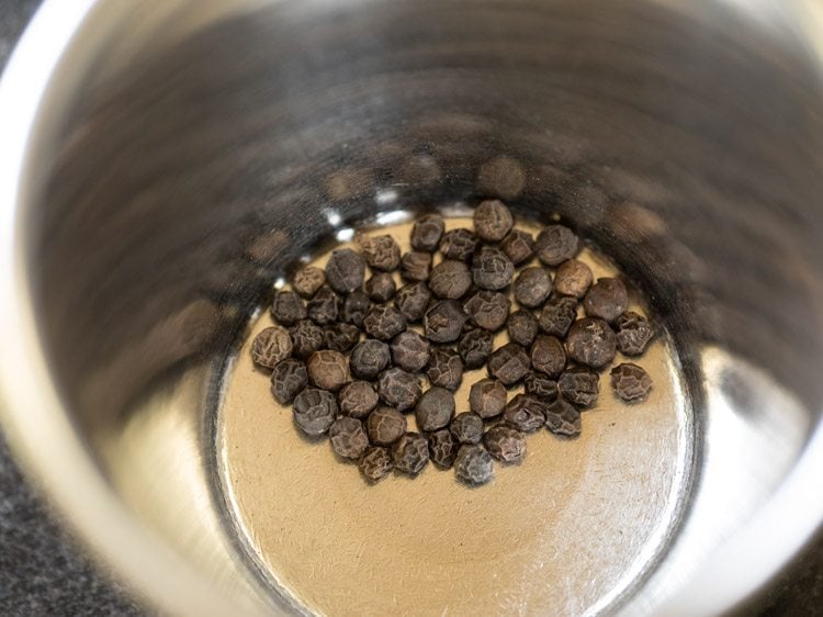 whole black pepper added to a mortar. 