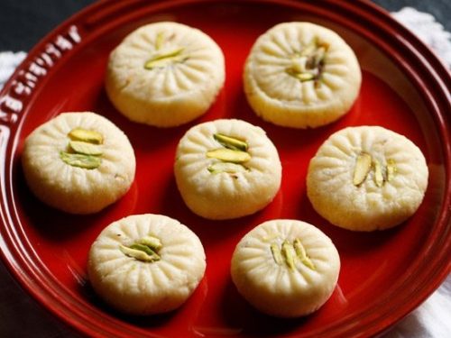 7 peda pieces on a red plate placed on white doilies.