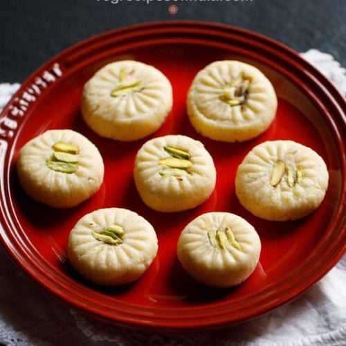 7 peda pieces on a red plate placed on white doilies.