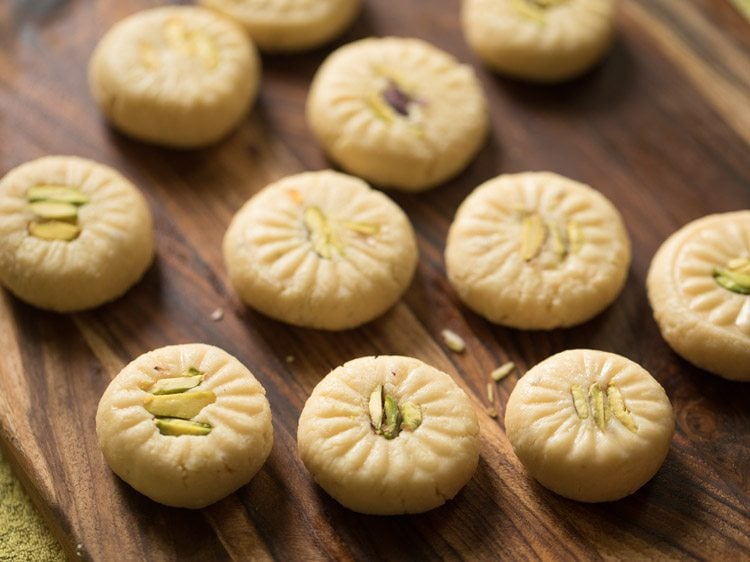 prepared peda with a petal design and pistachio slivers in the center placed on wooden board