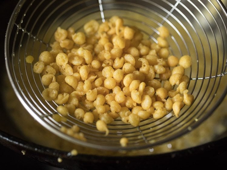 removing fried boondi from oil using a slotted spoon. 