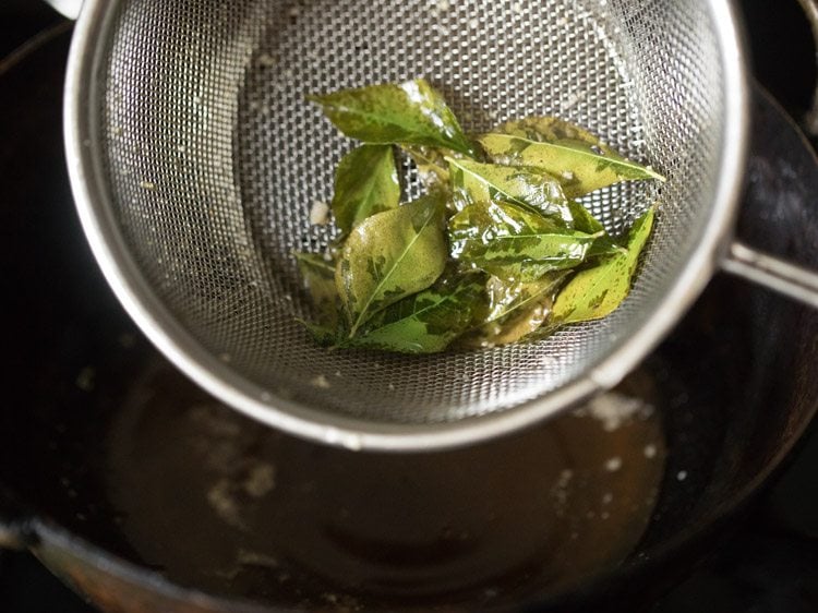 frying curry leaves in sieve ladle till crisp. 