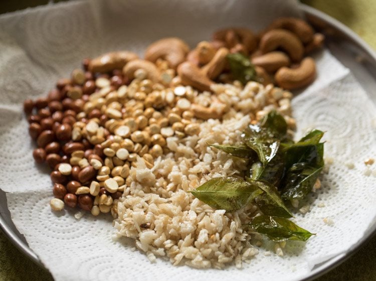 fried curry leaves kept with fried poha, fried chana dal, fried cashews and fried peanuts on kitchen paper towels. 