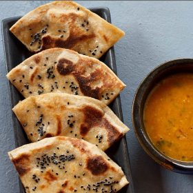 cheese naan wedges served on a black platter with a bowl of curry kept on the right side and text layovers.