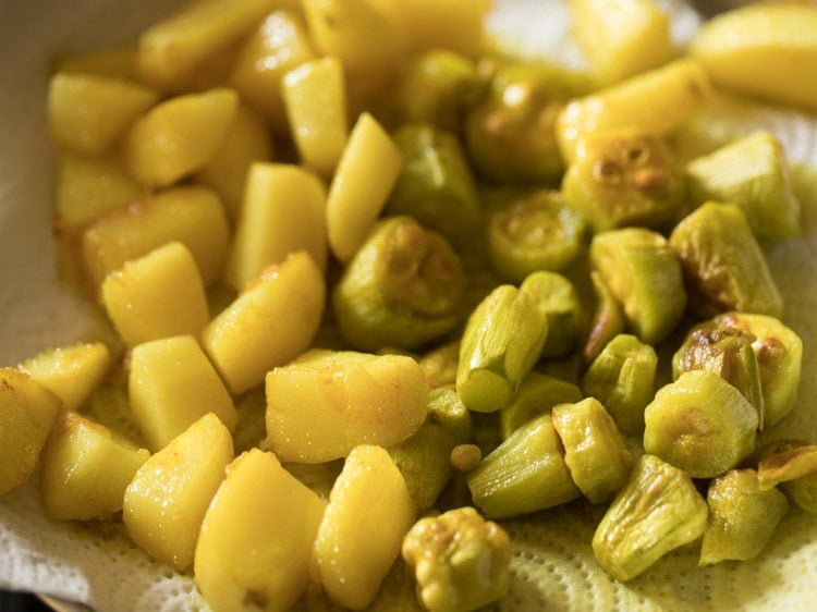 fried potato cubes kept on kitchen paper towel with fried pointed gourd pieces. 