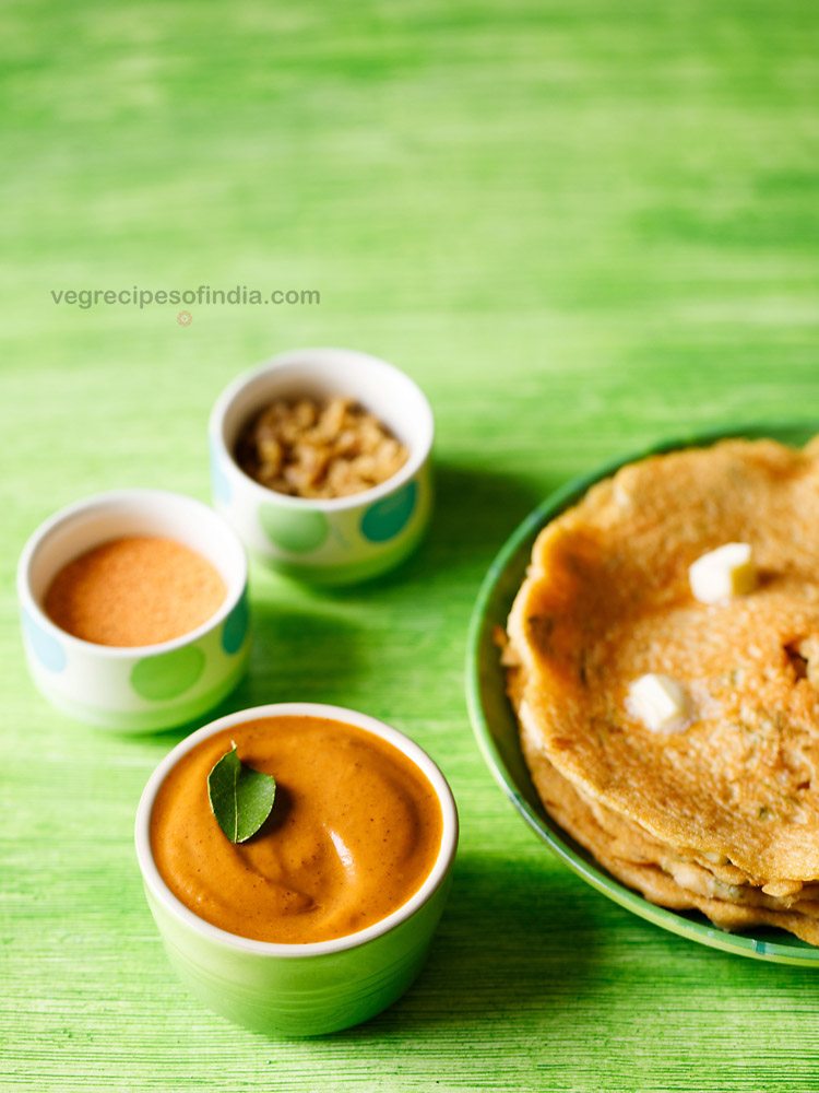 tomato pachadi garnished with a curry leaf, served in a light green colored small bowl with dosas kept on a light green colored platter and text layovers.
