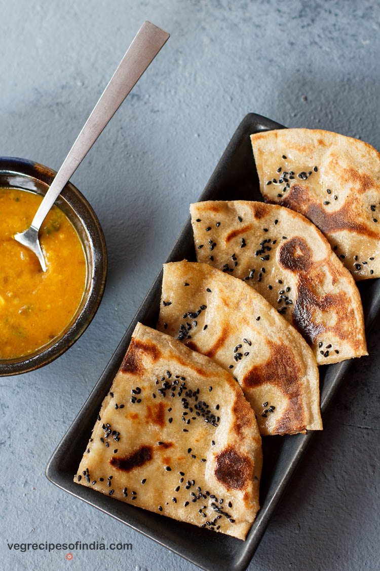 cheese naan wedges served on a black platter with a bowl of curry kept on the left side. 