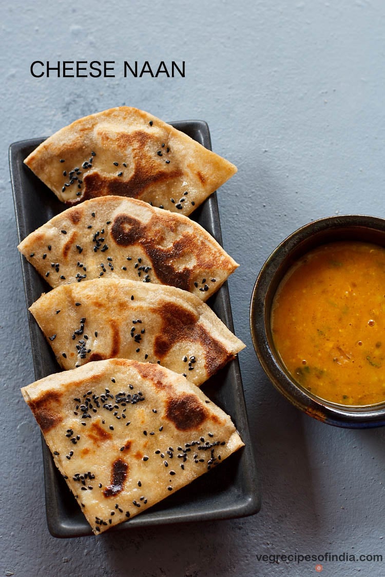 cheese naan wedges served on a black platter with a bowl of curry kept on the right side and text layover.