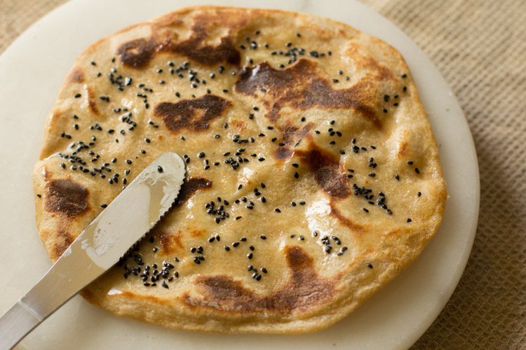 spreading butter on roasted cheese naan. 