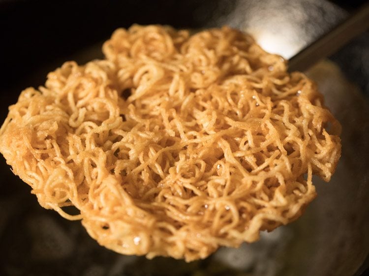 removing fried noodles from hot oil using a slotted spoon. 