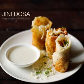 jini dosa garnished with grated cheese and served on a white plate with a bowl of coconut chutney kept on the left side on the plate and text layovers.