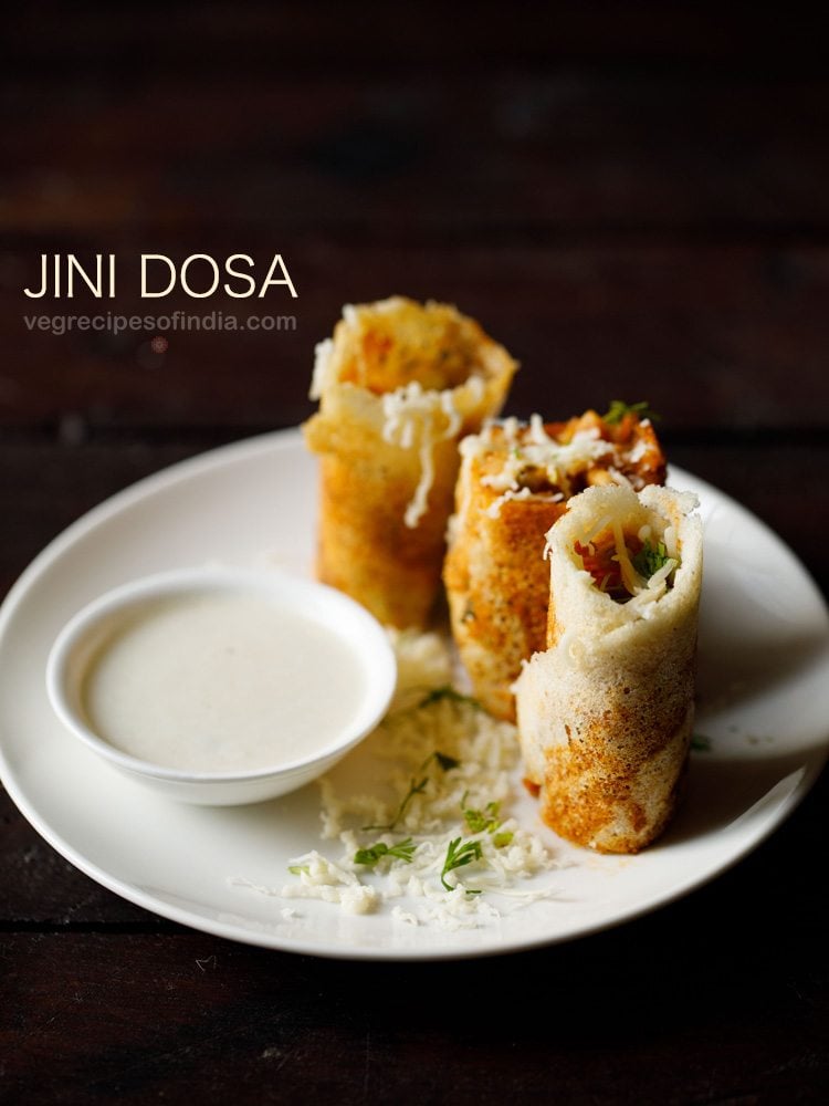 jini dosa garnished with grated cheese and served on a white plate with a bowl of coconut chutney kept on the left side on the plate and text layovers.
