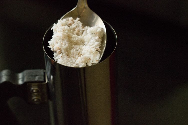 adding fresh grated coconut in the cylindrical vessel of kudam. 