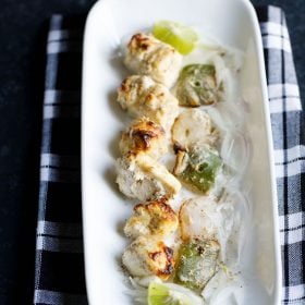 paneer malai tikka served on a rectangular white platter with sliced onion and lemon wedges, and text layover.