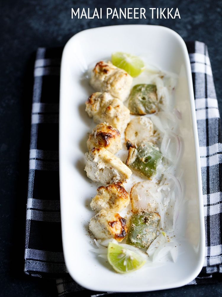 paneer malai tikka served on a rectangular white platter with sliced onion and lemon wedges, and text layover.
