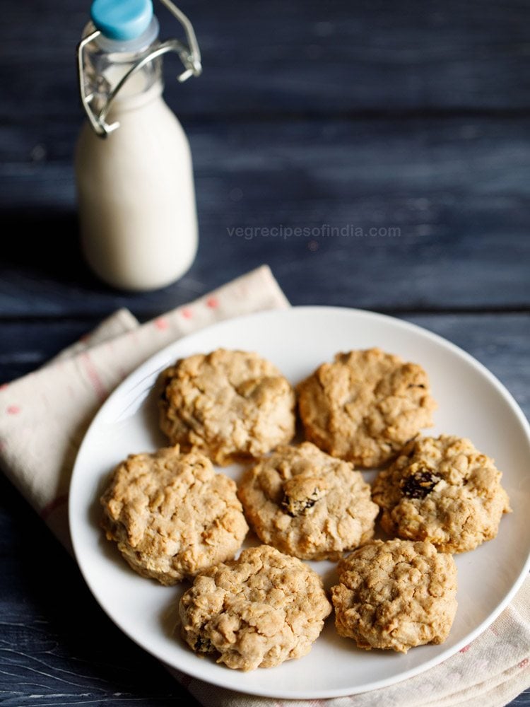 single oatmeal cookies kept on a white plate on a cream napkin with a small glass bottle of milk in the background 