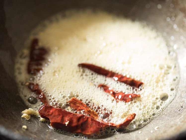 Chopped garlic and red chili being fried in a pan.