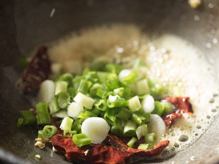 Chopped garlic, red chili and spring onion being fried in a pan.