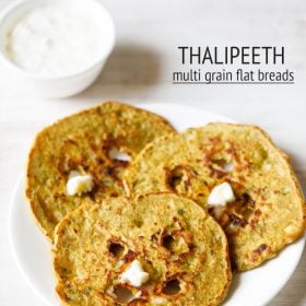 thalipeeth topped with white butter and served on a white plate with a bowl of curd kept on the top left side and text layovers.